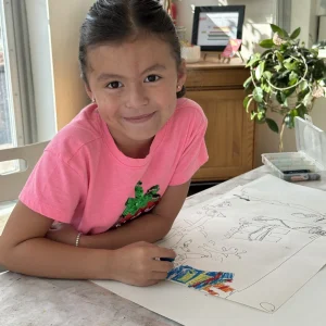 A young student smiling while working on a colorful drawing during the Summer Camp Basics of Drawing class