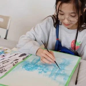 Teen student painting a blue watercolor landscape during art class at Aliki’s Art House.